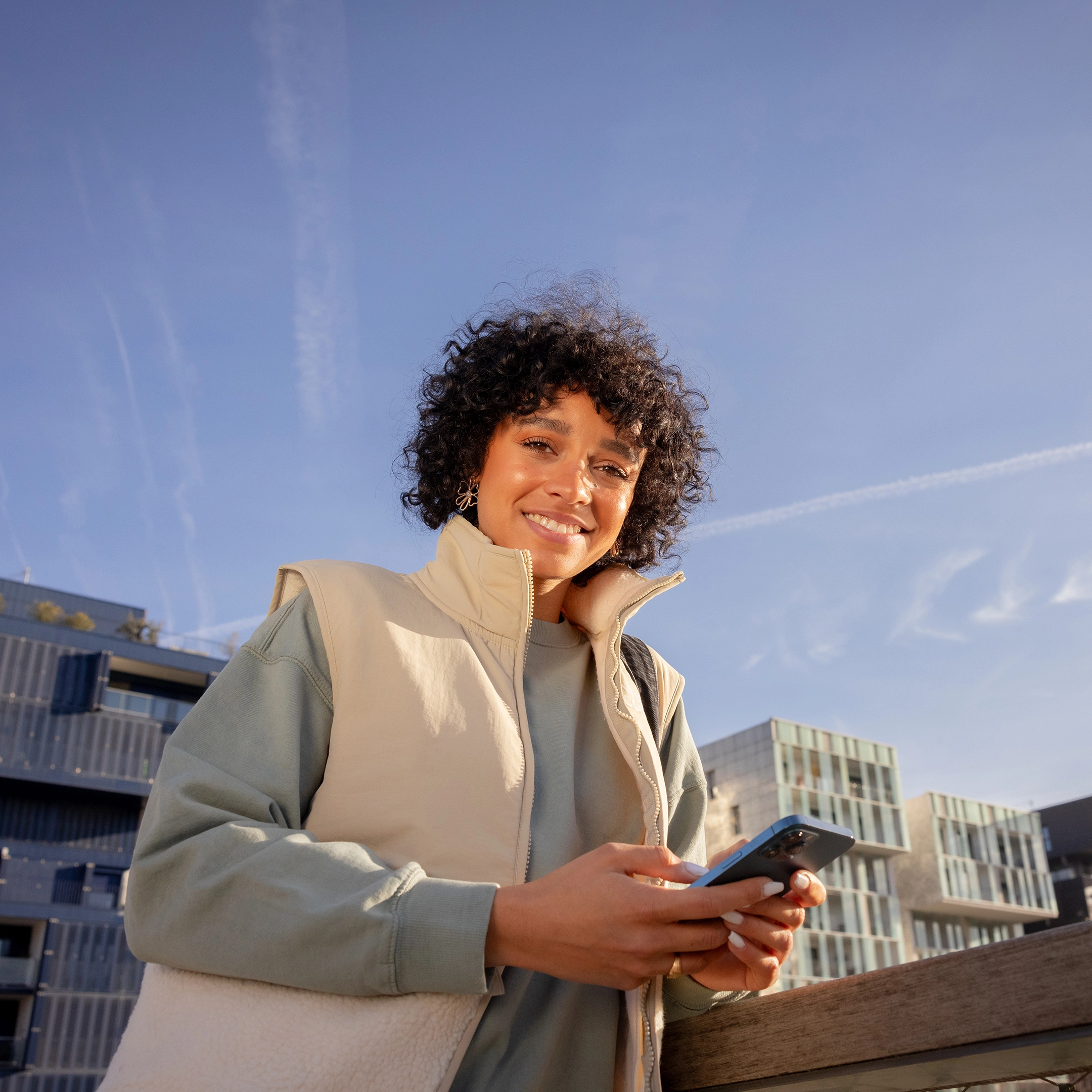 Une jeune femme en contre-plongée dans un décor moderne utilise son portable et nous sourit.